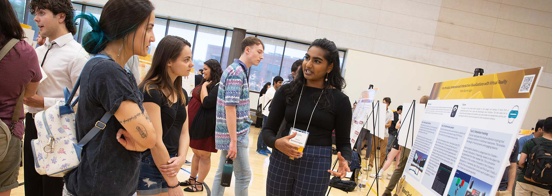 A student presents her research findings to a couple of people at a research presentation poster session.