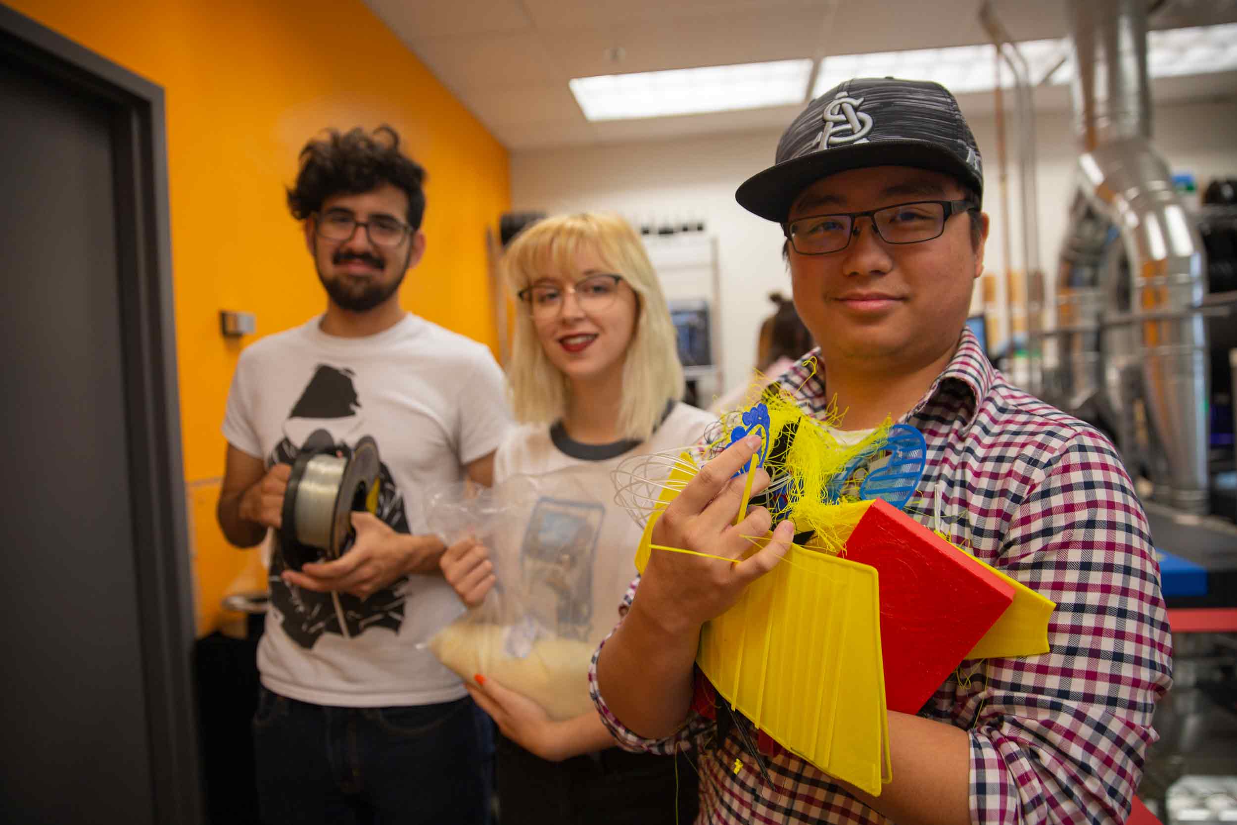 Three Arizona State University engineering students pose for a photo while holding materials which can be recycled in the 3D Print Lab
