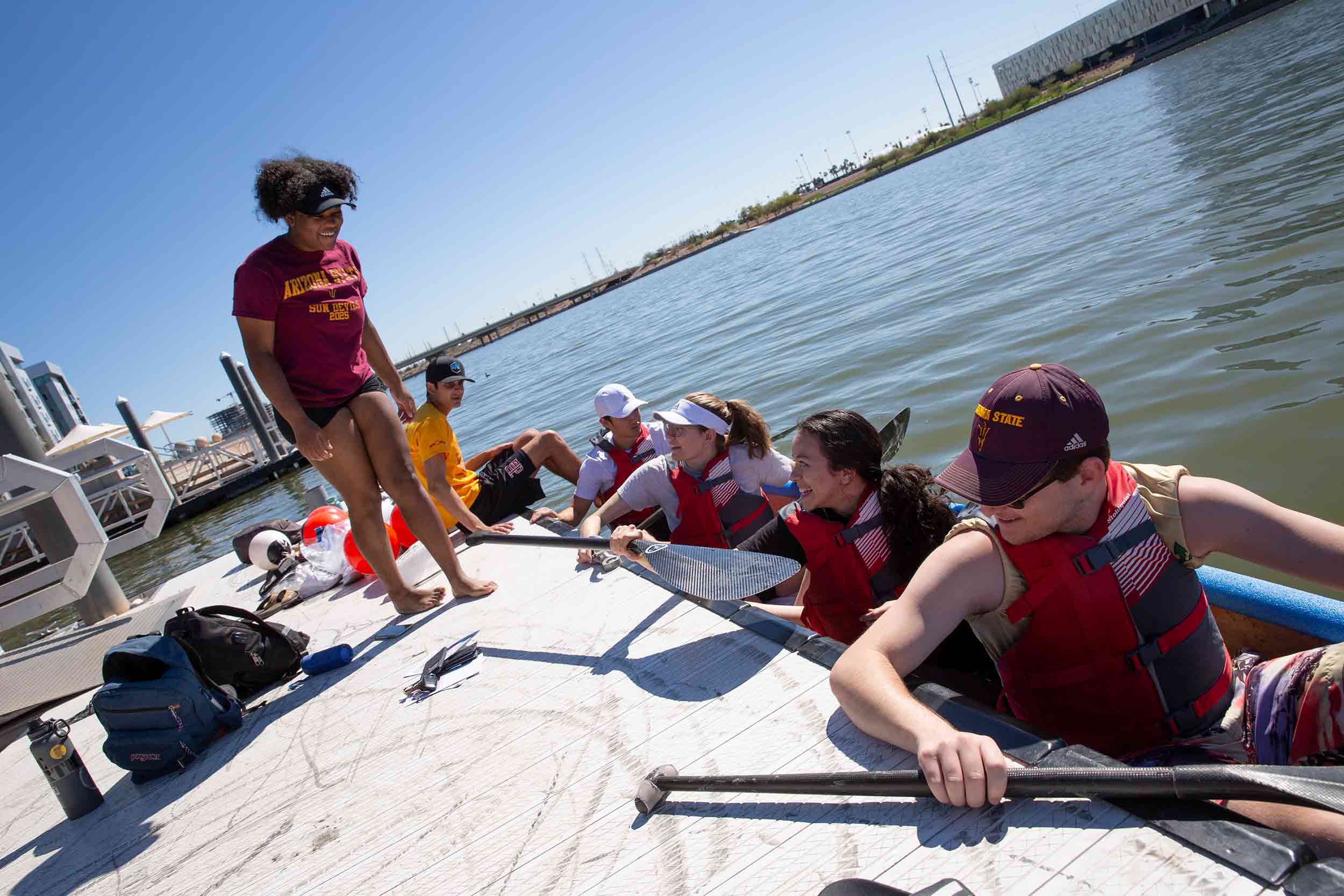 Members of the ASU student chapter of ASCE are lined up on a canoe, with one member on the deck next to them, in Tempe Town Lake.