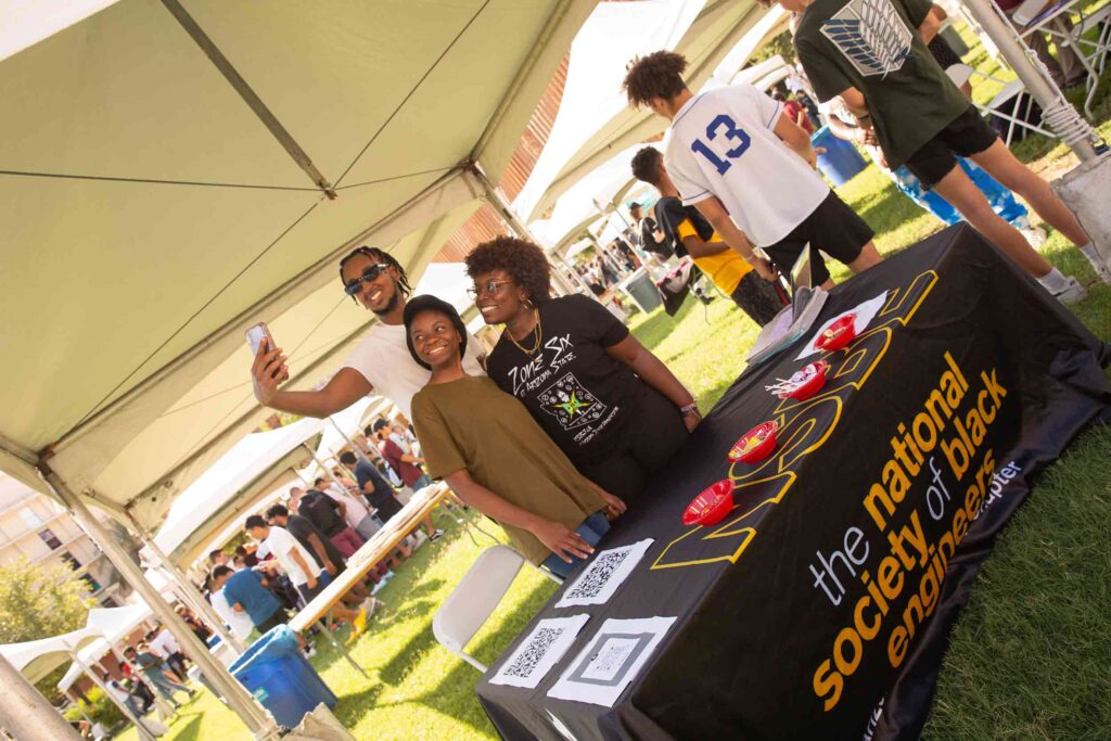 Three members of the ASU student chapter of the National Society of Black Engineers (NSBE) stand together for a selfie at an ASU student org fair.