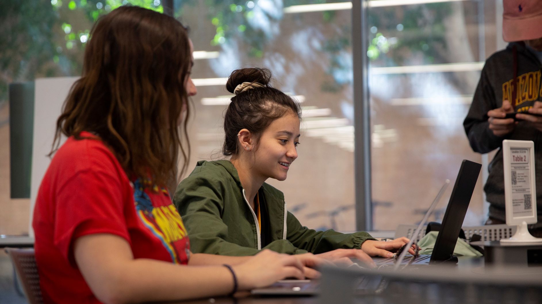 Two students studying collaboratively at a table with papers and a laptop with a Fulton Schools tutor guiding them in their work.
