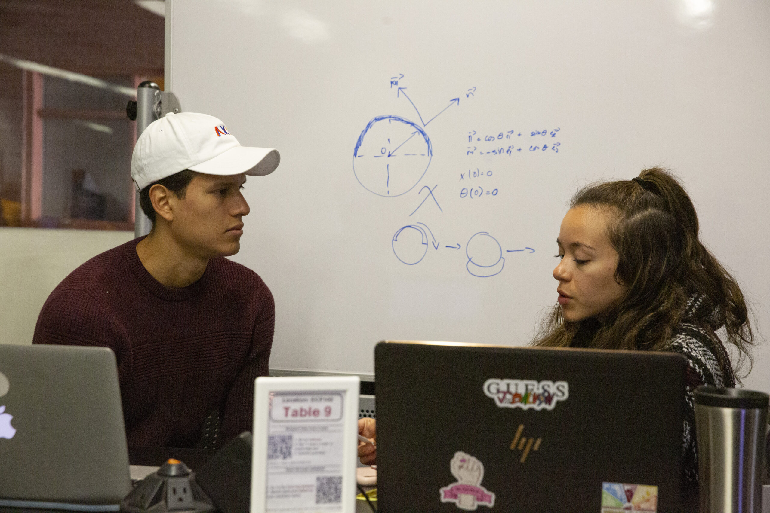 A tutor sits at a white board explaining a math problem to two students.