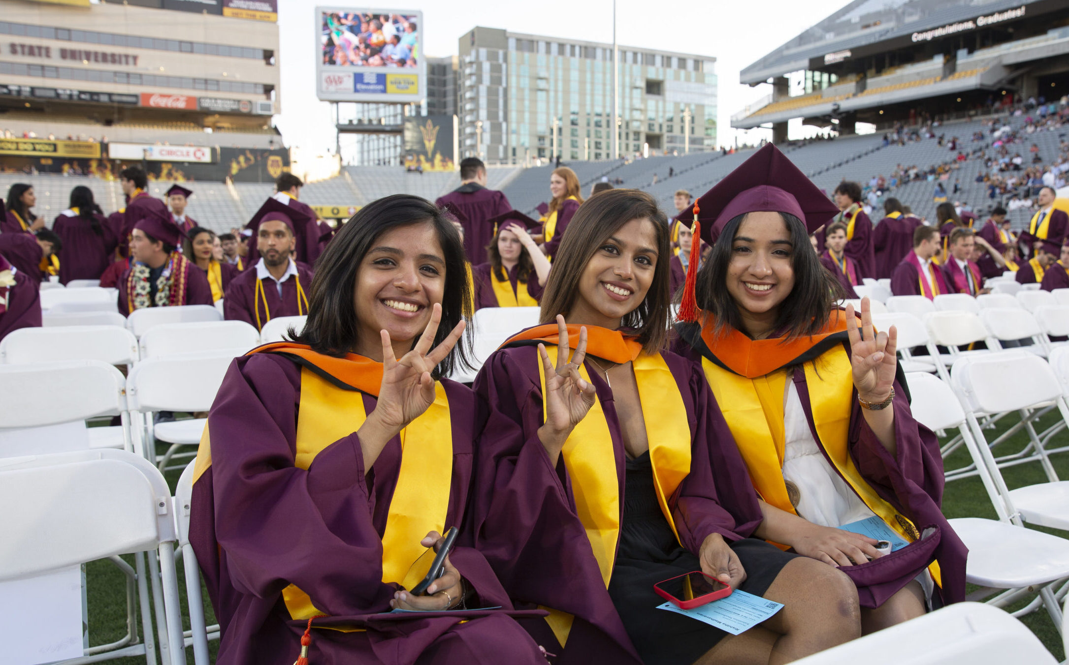 A group of three international women graduates sit at Convocation in their regalia, smiling for the camera.