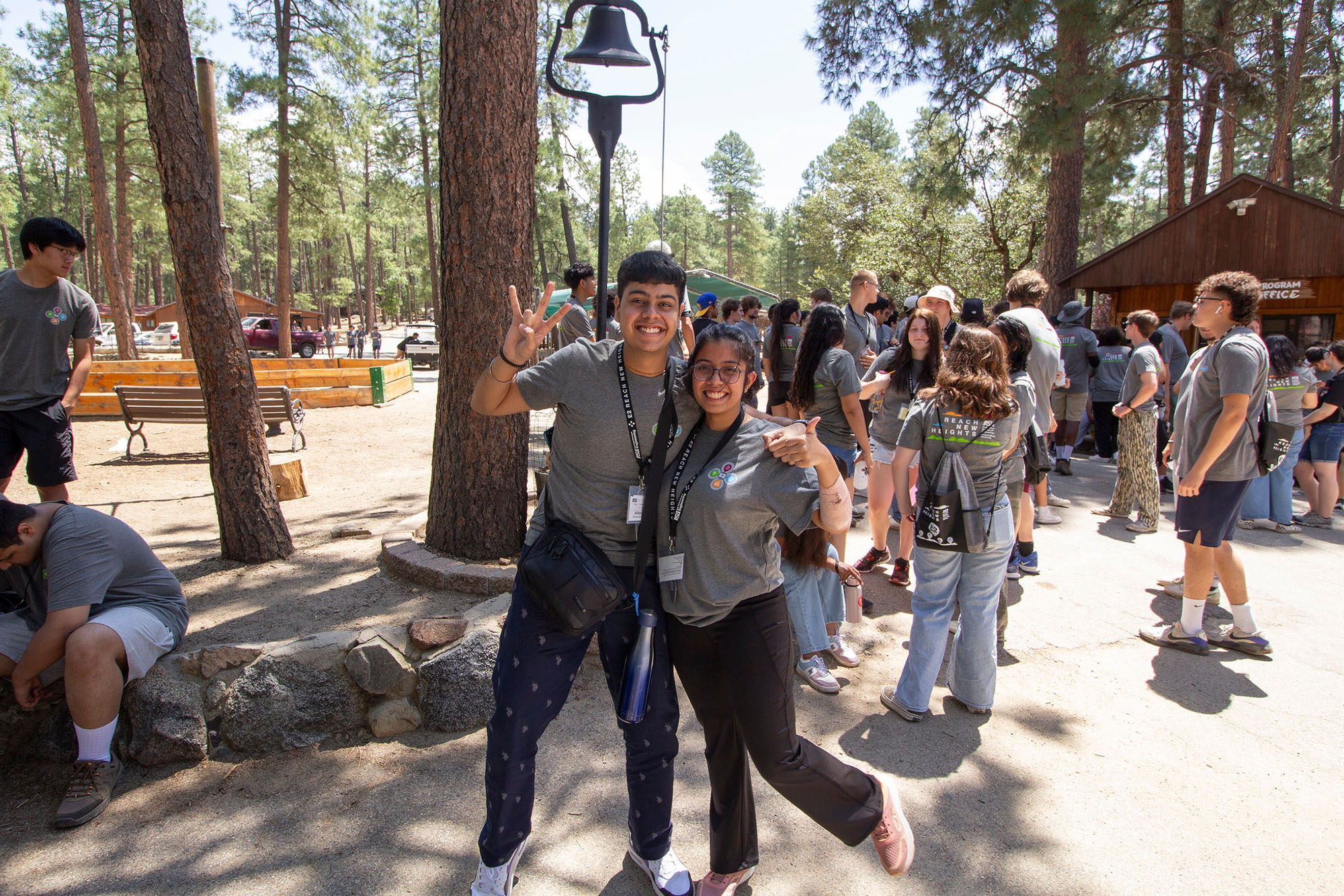 Two students pose with the fork symbol held up at a campground with lots of trees behind them.