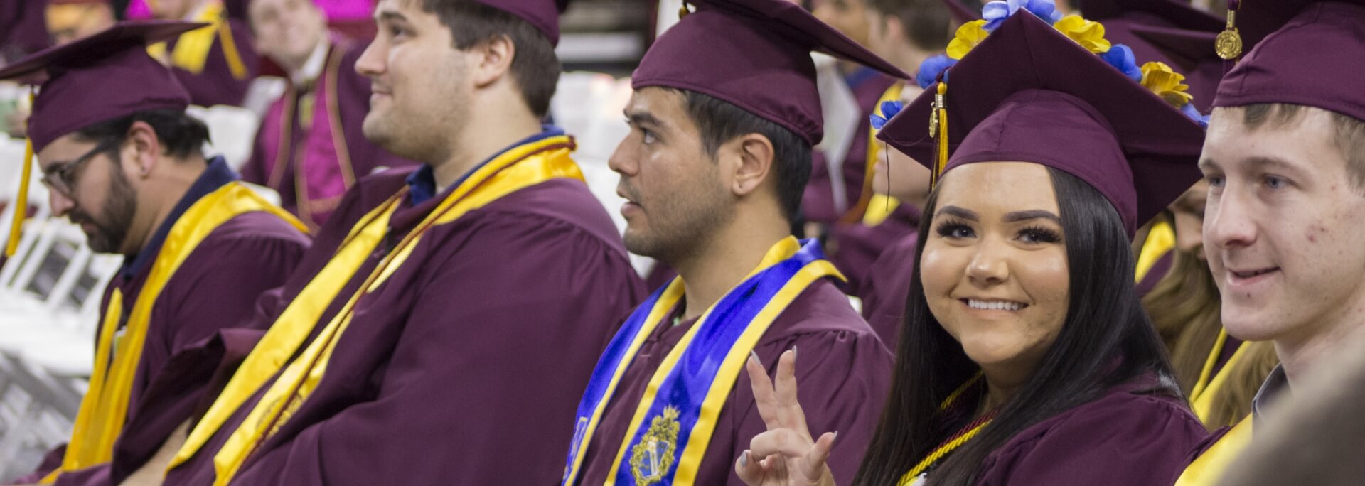 A student looks at the camera and smiles at convocation wearing her graduation cap and gown.