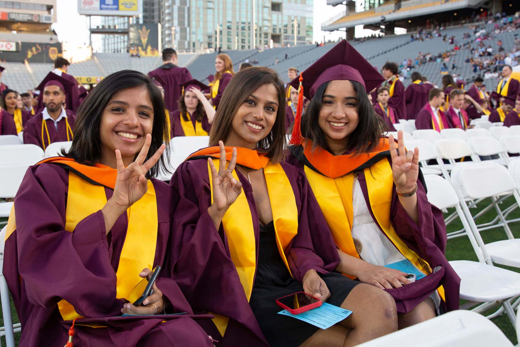 A group of three international women graduates sit at Convocation in their regalia, smiling for the camera.