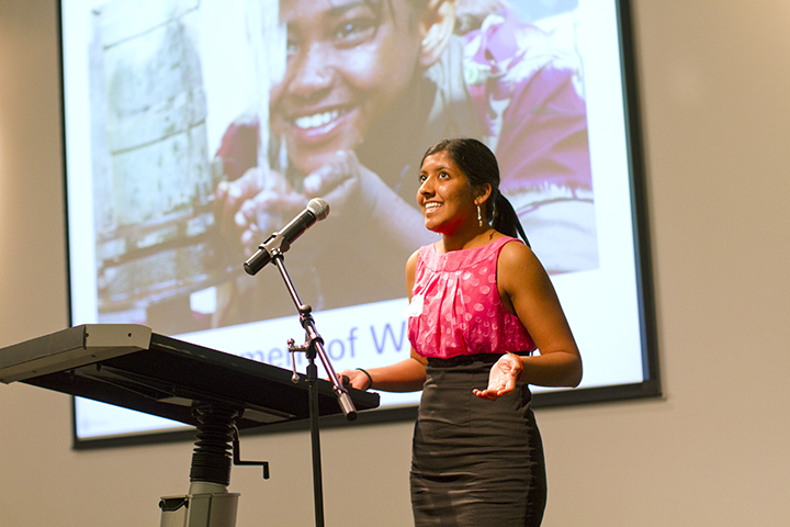 A student stands at a podium giving a talk about her research.