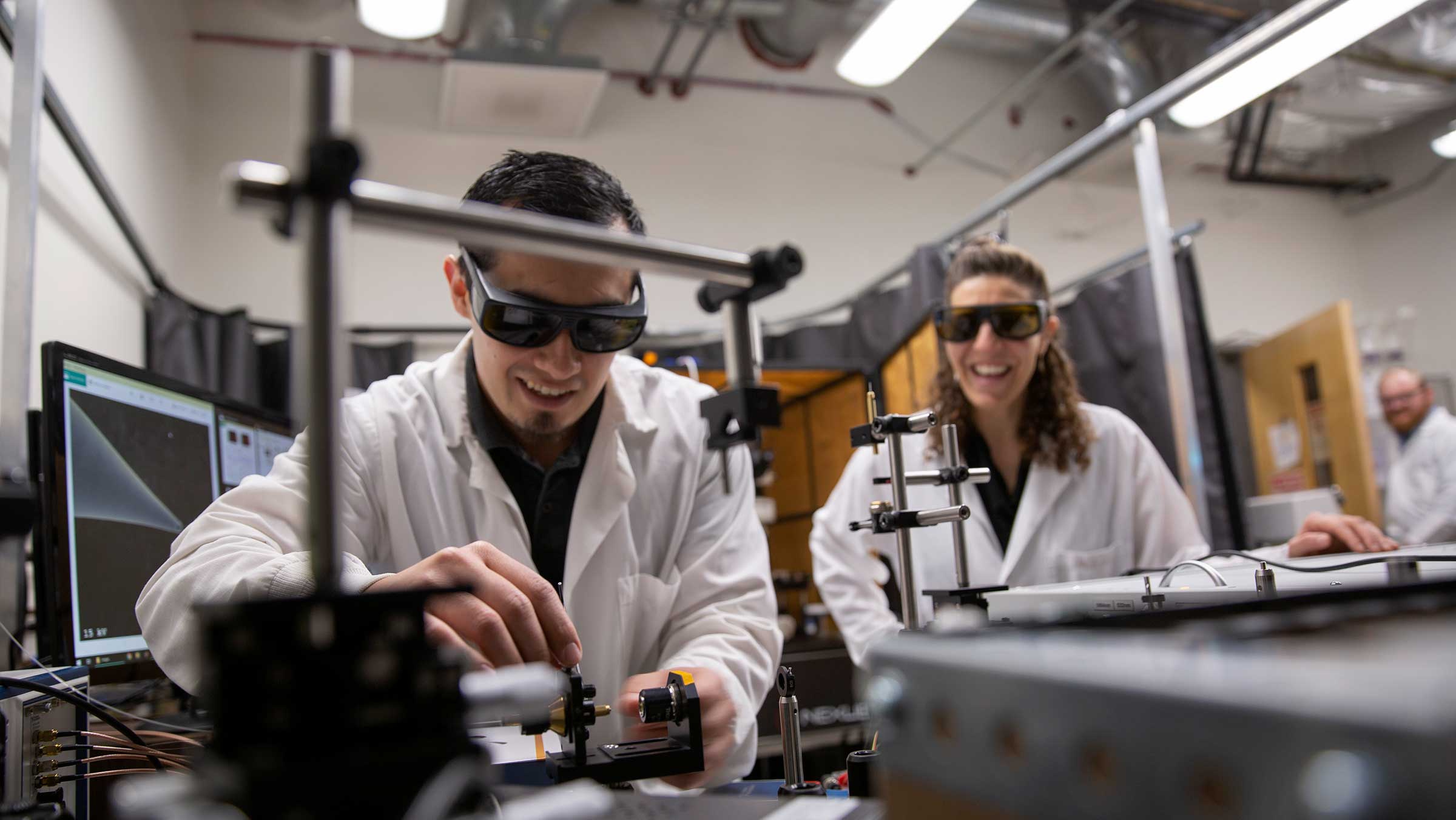 A graduate student in Barbara Smith works at the bench while Barbara looks on. Both are wearing protective clothing and dark glasses.