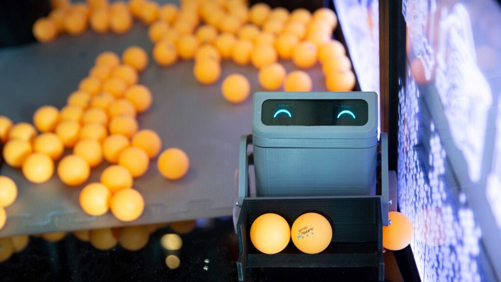 Small robot that can pick up ping-pong balls looks up at the camera with LED "smile eyes"