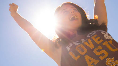 A woman wearing an ASU shirt puts her arms in the air in celebration