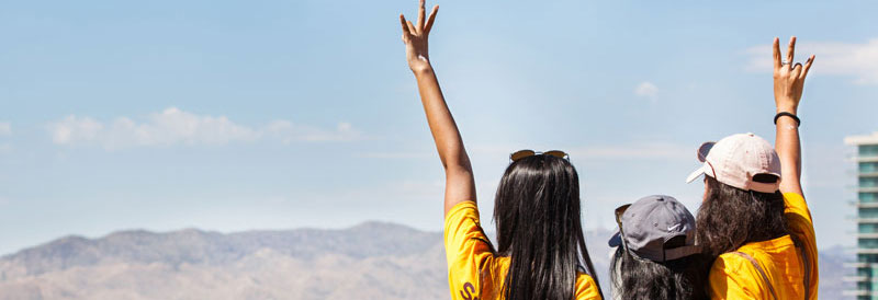 Three women stand atop A Mountain and throw up the fork hand signal.