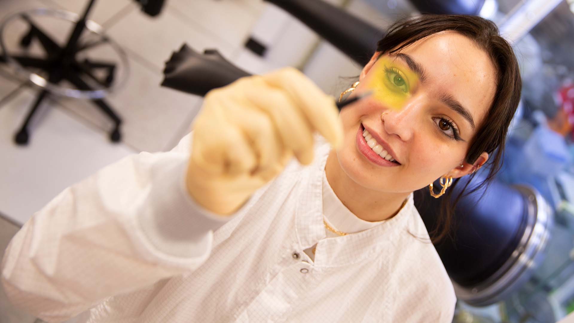 FURI student Clara Chaves Azevedo works in the lab, holding a small component with tweezers.