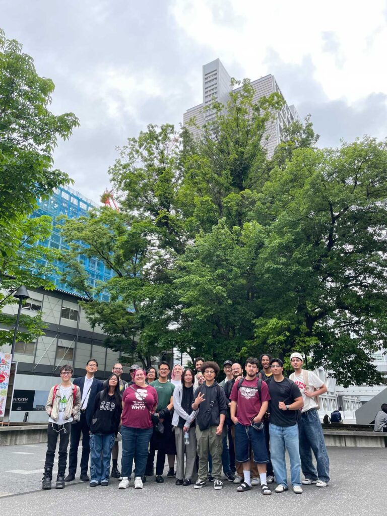 A group of students poses for a photo in front of trees and buildings in Japan
